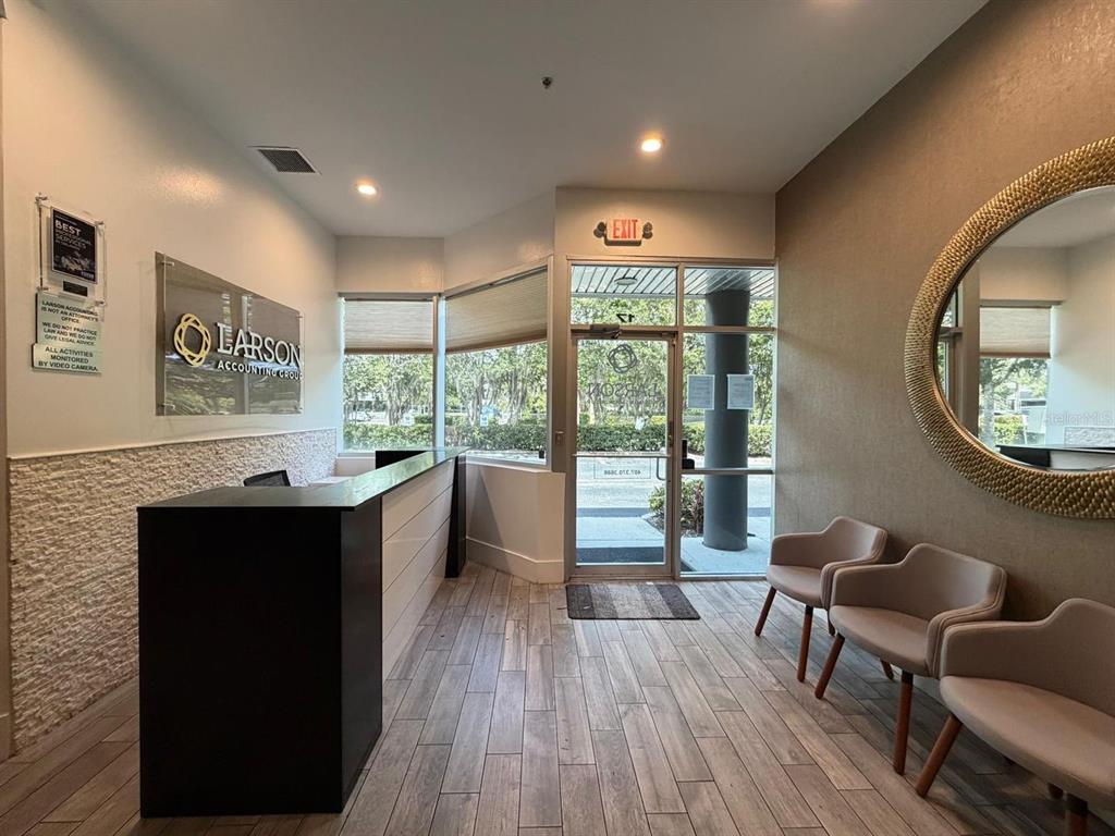 A reception area features a dark desk, three chairs, a large mirror, and glass doors — 7901 KINGSPOINTE PARKWAY UNIT 16 and 17, ORLANDO, FL