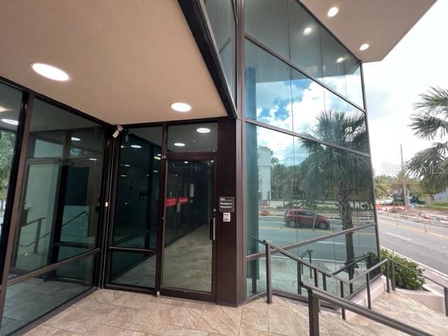 The exterior entrance of a modern office building features glass walls and a tiled walkway — 1118 S ORANGE AVENUE UNIT 104, ORLANDO, FL