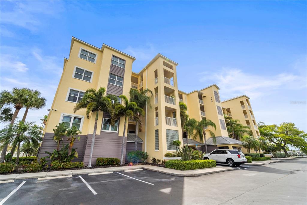 A multi-story yellow apartment building with palm trees and a parking lot in front — 425 150TH AVENUE UNIT 2303, MADEIRA BEACH, FL