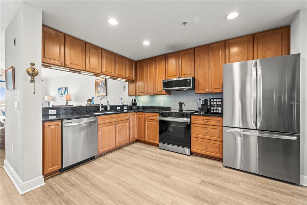 A kitchen features wood cabinets, stainless steel appliances, dark countertops, and light wood-look flooring — 425 150TH AVENUE UNIT 2303, MADEIRA BEACH, FL
