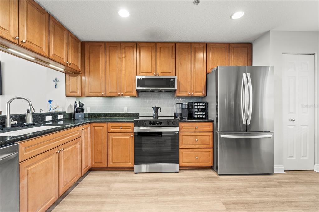 A kitchen features wood cabinets, stainless steel appliances, dark countertops, and light wood-look flooring — 425 150TH AVENUE UNIT 2303, MADEIRA BEACH, FL