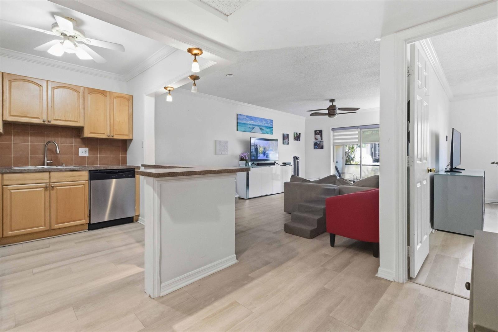 A kitchen with wood cabinets and a stainless dishwasher opens to a living area — 259 S Cypress Road # 506, Pompano Beach FL 33060, POMPANO BEACH, FL