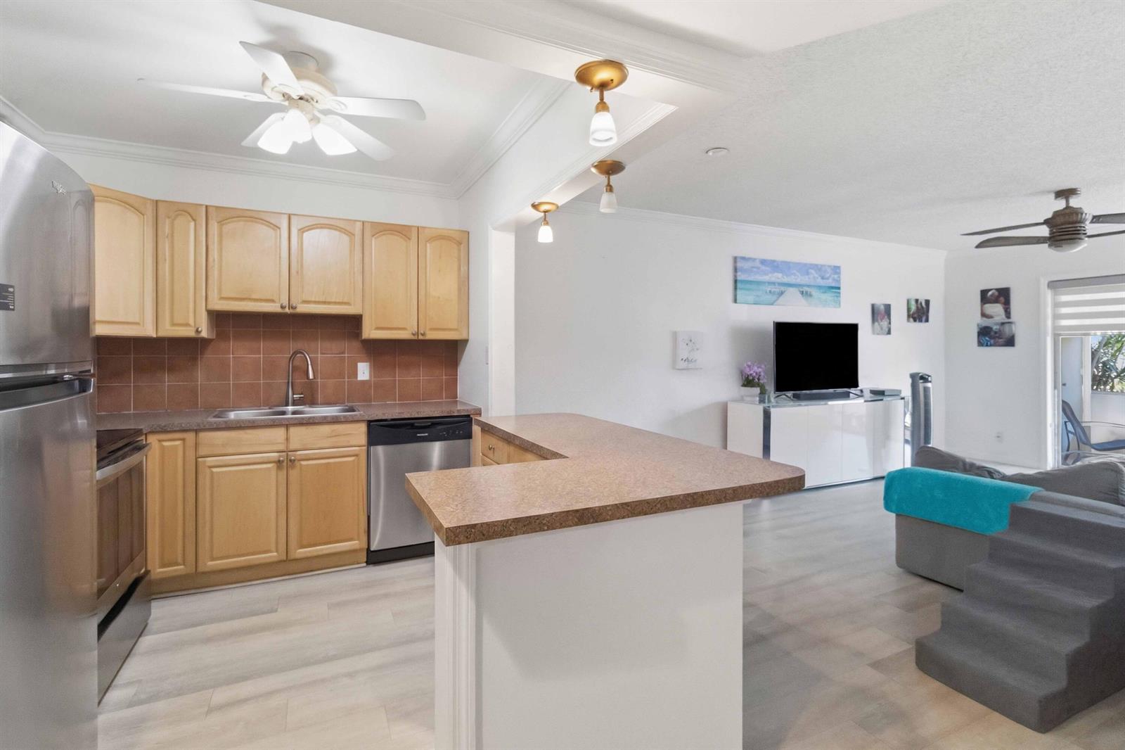 A kitchen with light wood cabinets and a breakfast bar overlooks a living room area — 259 S Cypress Road # 506, Pompano Beach FL 33060, POMPANO BEACH, FL