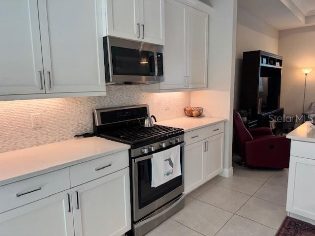 A modern kitchen features white cabinetry, stainless steel appliances, and a tiled backsplash — 6224 CHAMPIONS ROW STREET, BRADENTON, FL