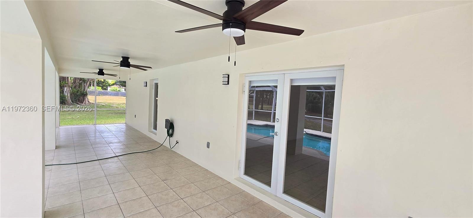 A covered patio features light tile flooring, ceiling fans, and glass doors overlooking a pool — 6500 SW 82nd Ave, Miami FL 33143, MIAMI, FL