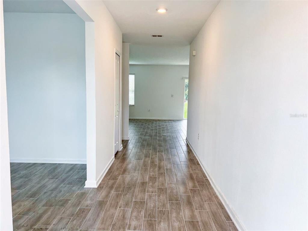 A hallway with wood-look tile flooring leads to an open living area with a window — 5030 FOUR STRAND COURT, ST CLOUD, FL