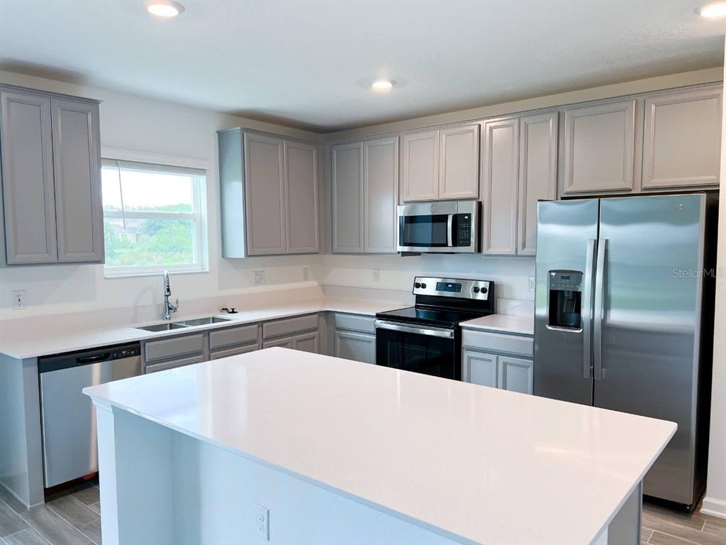 A kitchen features gray cabinets, stainless steel appliances, and a white quartz island countertop — 5030 FOUR STRAND COURT, ST CLOUD, FL