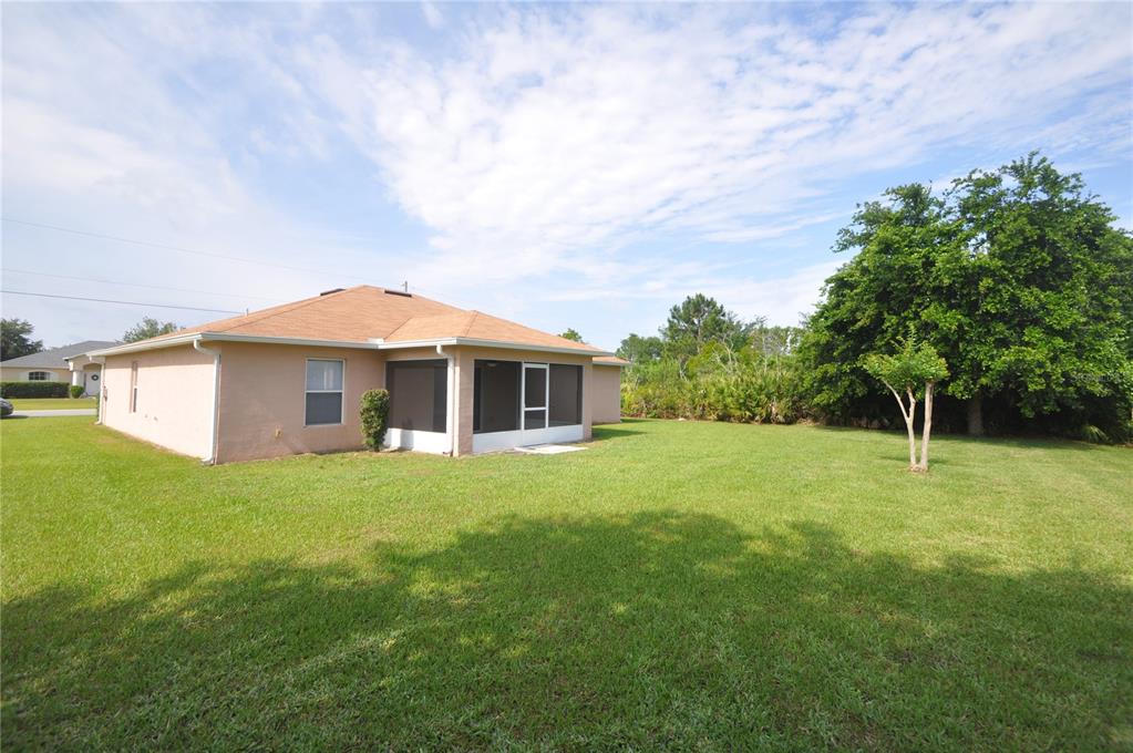 A tan house with a screened-in porch sits on a large, grassy backyard lot — 37 LOUISBURG LANE, PALM COAST, FL