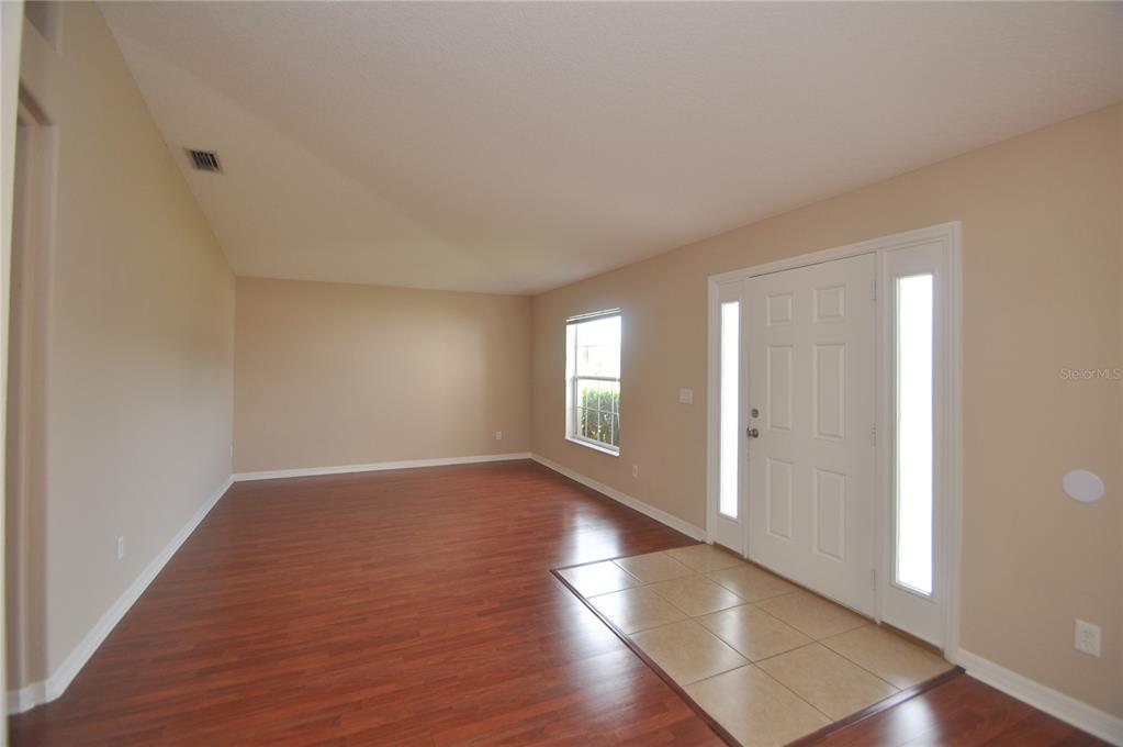 An empty room with wood-look flooring, a tiled entryway, and a white front door — 37 LOUISBURG LANE, PALM COAST, FL