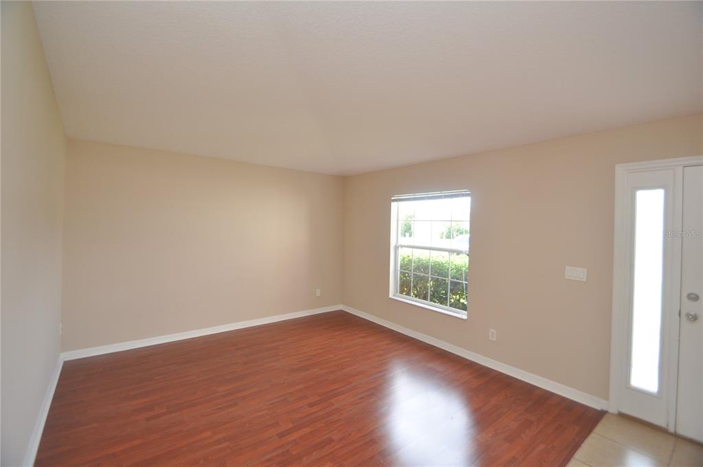 An empty room features wood-look flooring, beige walls, a single window, and a white front door — 37 LOUISBURG LANE, PALM COAST, FL