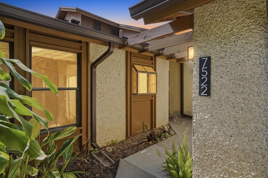 A concrete walkway leads to the front entrance of a house with textured stucco walls — 7522 4TH AVENUE W, BRADENTON, FL