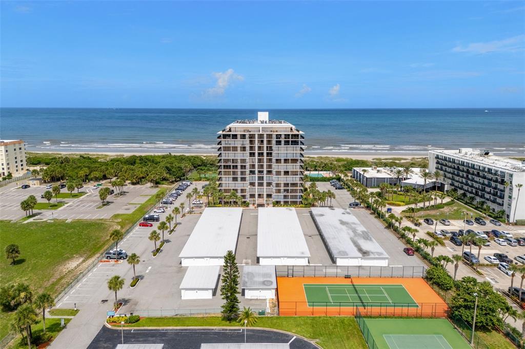 An aerial view shows a tall beachfront condominium building with parking lots and tennis courts — 2100 N ATLANTIC AVENUE UNIT 502, COCOA BEACH, FL