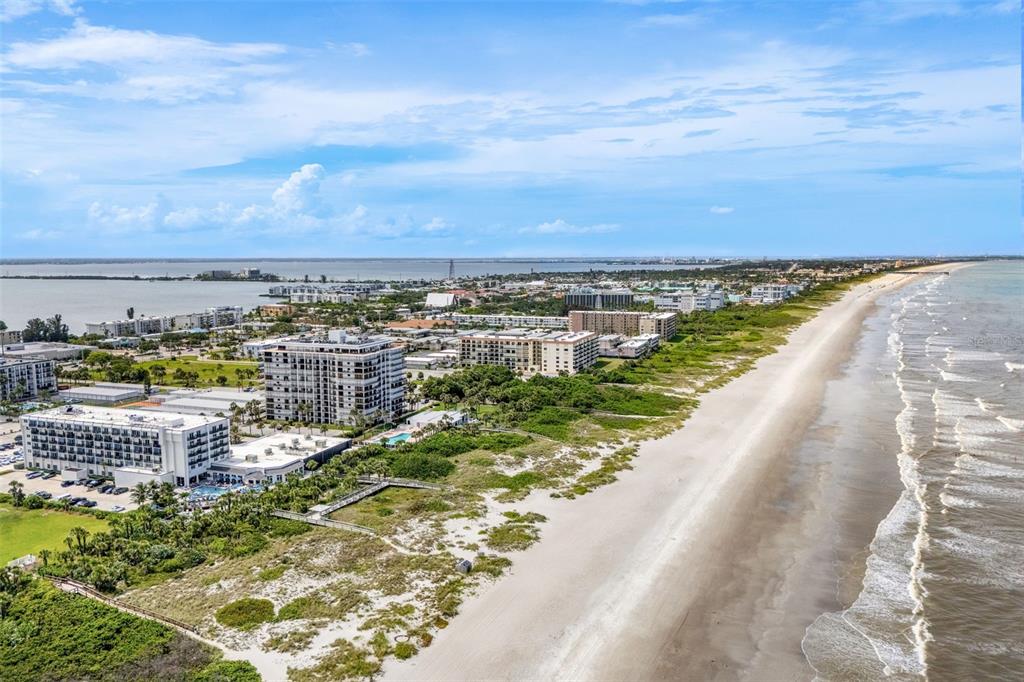 An aerial view shows a sandy beach bordering a coastline with several multi-story apartment buildings — 2100 N ATLANTIC AVENUE UNIT 502, COCOA BEACH, FL