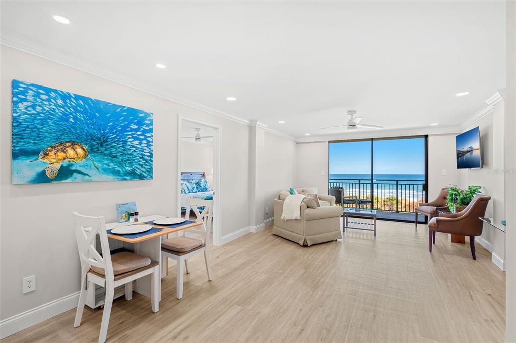 A bright living and dining area with light wood floors, ocean views, and a turtle painting — 2100 N ATLANTIC AVENUE UNIT 502, COCOA BEACH, FL
