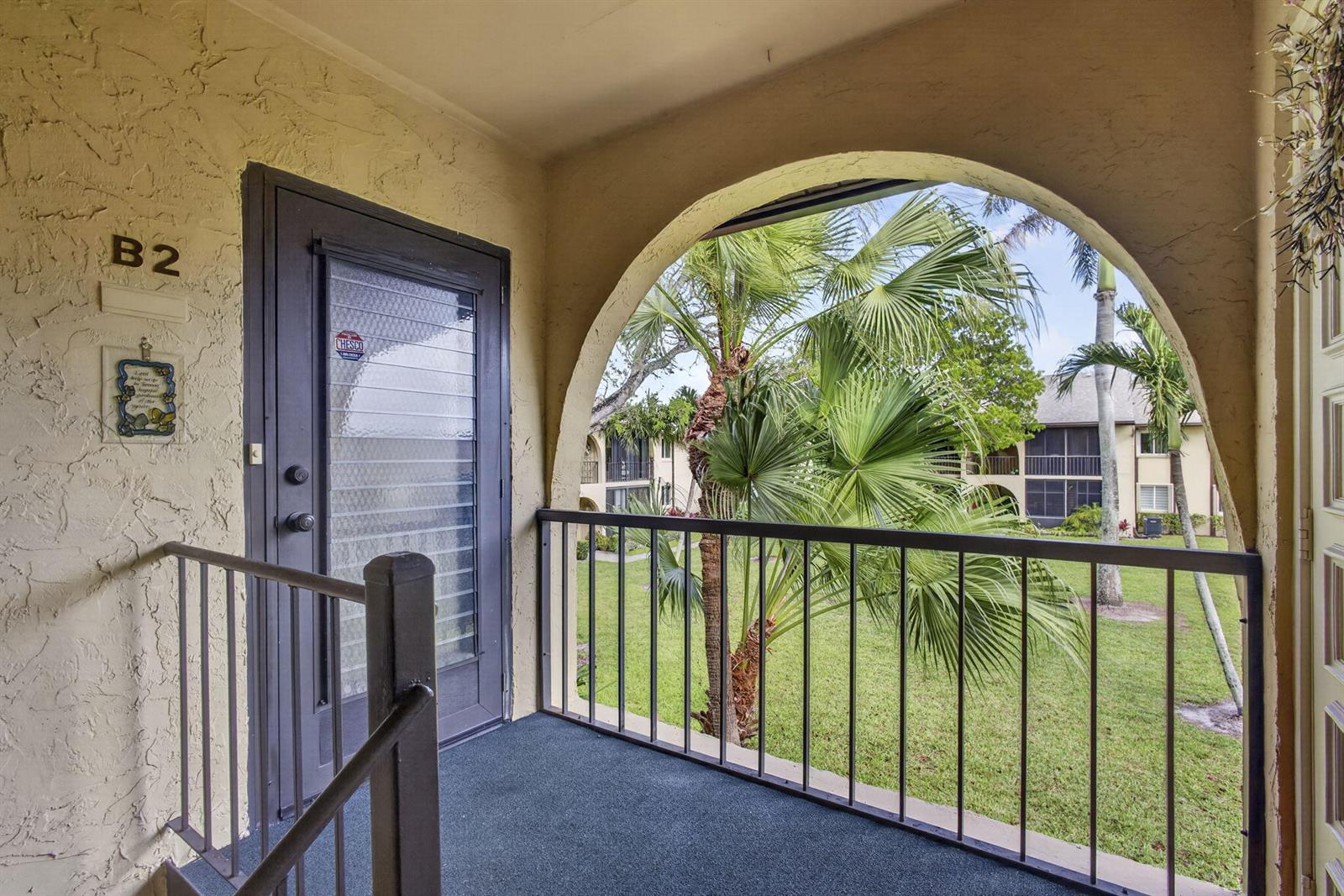 An apartment balcony with a dark metal railing, a glass-paneled door, and palm tree views — 301 Pine Ridge Circle # 2, FL 33463, FL