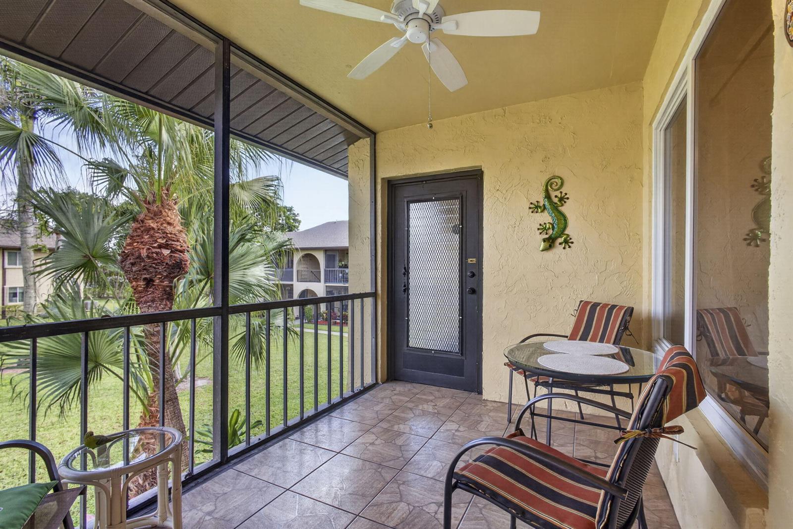 A screened-in balcony features tiled flooring, a ceiling fan, outdoor furniture, and a metal door — 301 Pine Ridge Circle # 2, FL 33463, FL
