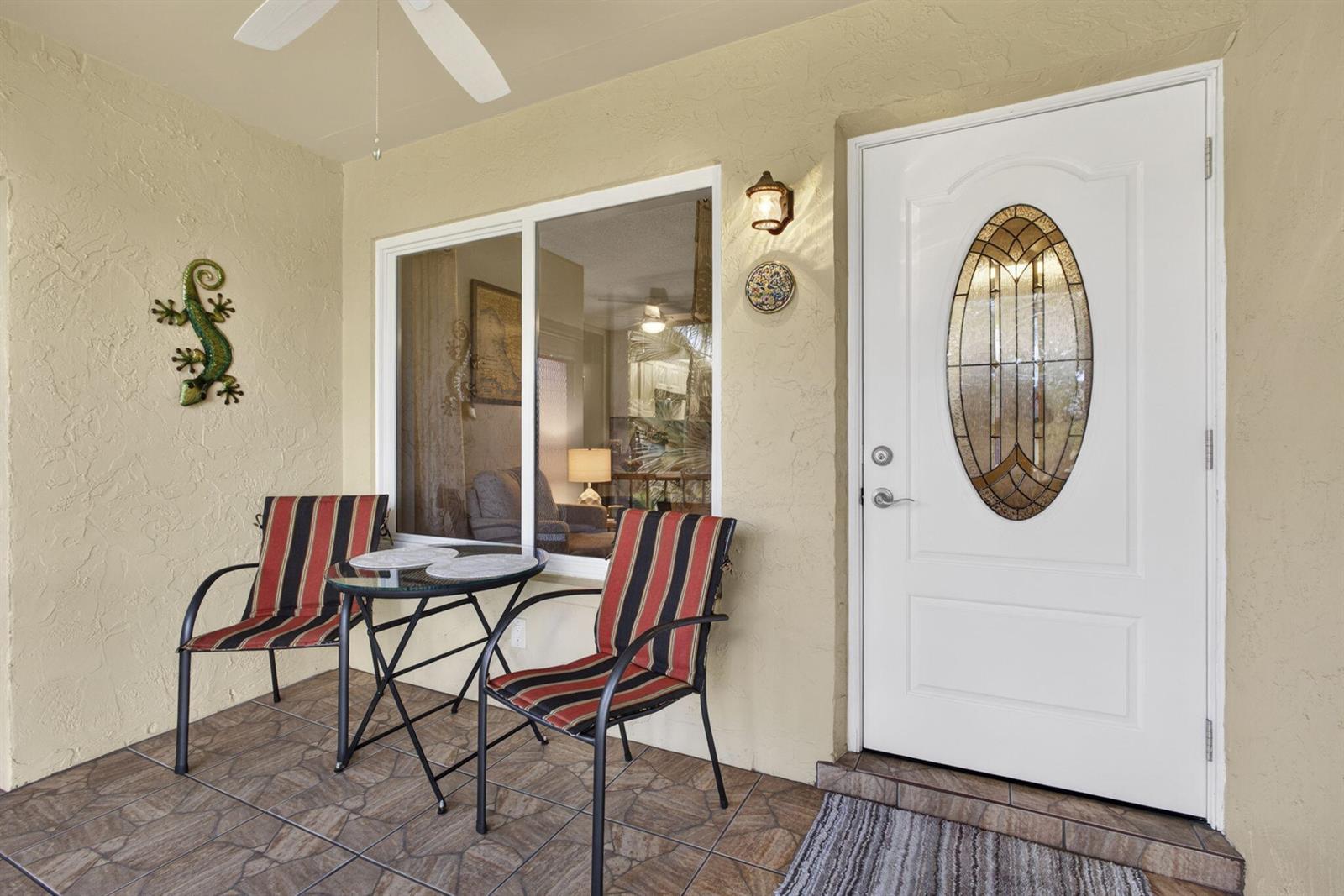A covered patio features a glass-topped table, two striped chairs, and a white front door — 301 Pine Ridge Circle # 2, FL 33463, FL