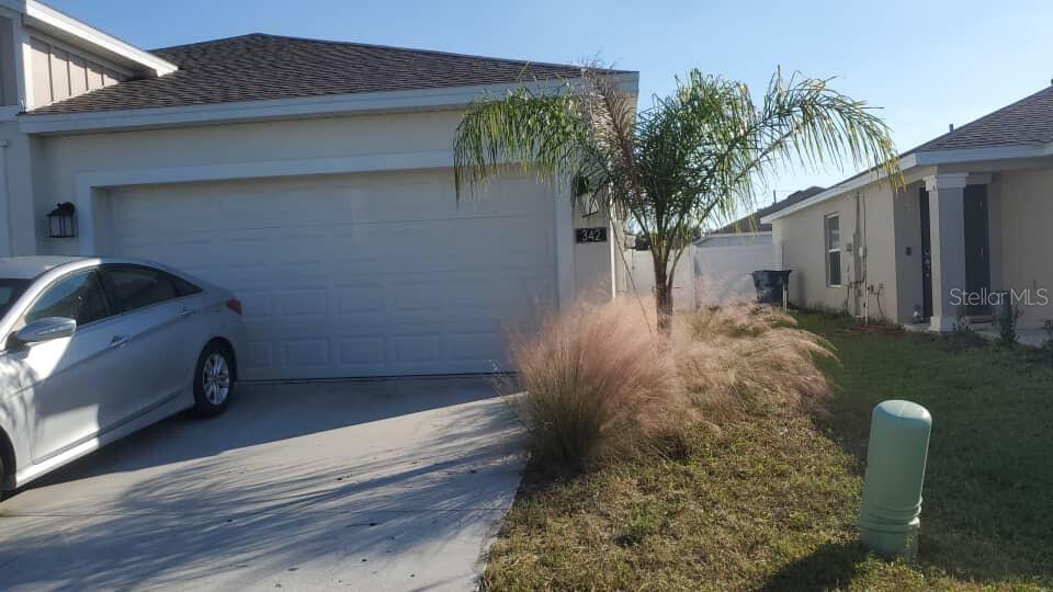 A silver sedan is parked in the driveway of a single-story house with a garage — 342 RUSTIC RAIL DRIVE, LAKE WALES, FL