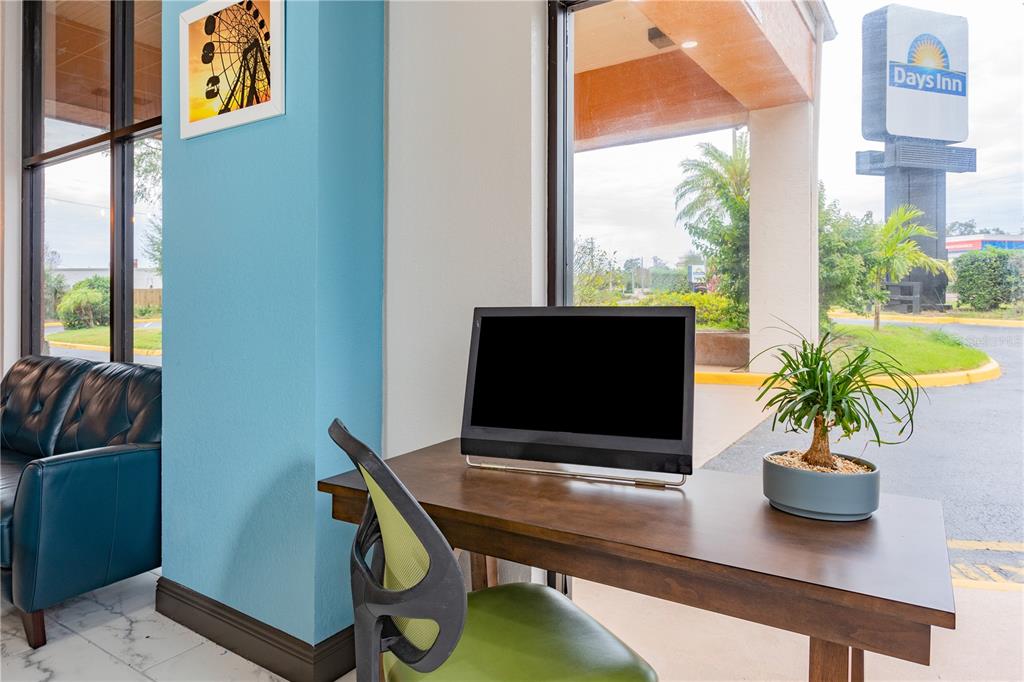 A hotel business center features a desk, computer monitor, chair, and a view of a sign — 8245 S US-17-92 HIGHWAY, CASSELBERRY, FL