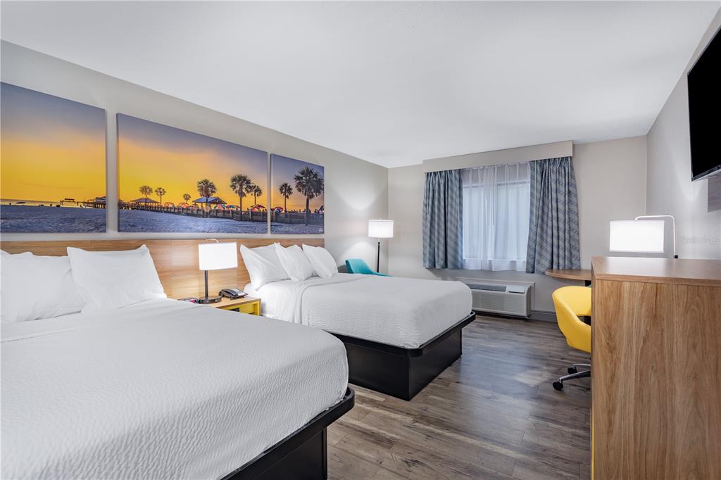 A hotel room features two queen beds, wood-look flooring, and a large sunset wall mural — 8245 S US-17-92 HIGHWAY, CASSELBERRY, FL