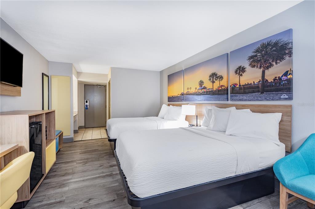 A hotel room features two beds, wood-look flooring, and wall art of a beach scene — 8245 S US-17-92 HIGHWAY, CASSELBERRY, FL