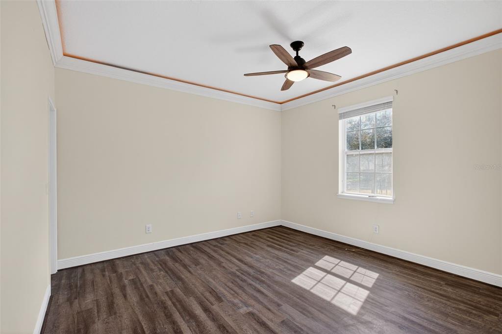 An empty bedroom features light-colored walls, dark wood-look flooring, crown molding, and a ceiling fan — 817 LOBELIA DRIVE, LAKE MARY, FL