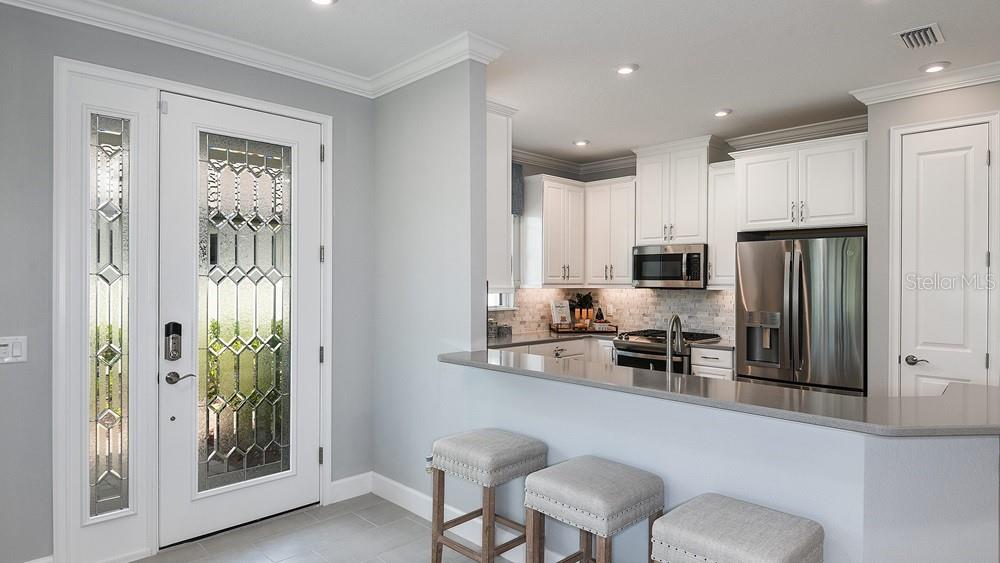 A kitchen with white cabinets and stainless steel appliances overlooks a breakfast bar with stools — 3224 TORTA COURT, BRADENTON, FL