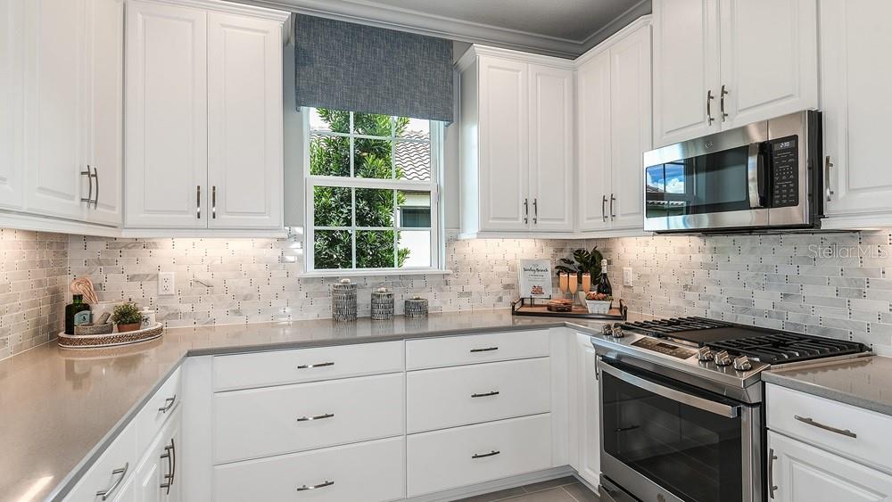 A kitchen features white cabinets, stainless steel appliances, and a gray tiled backsplash — 3224 TORTA COURT, BRADENTON, FL