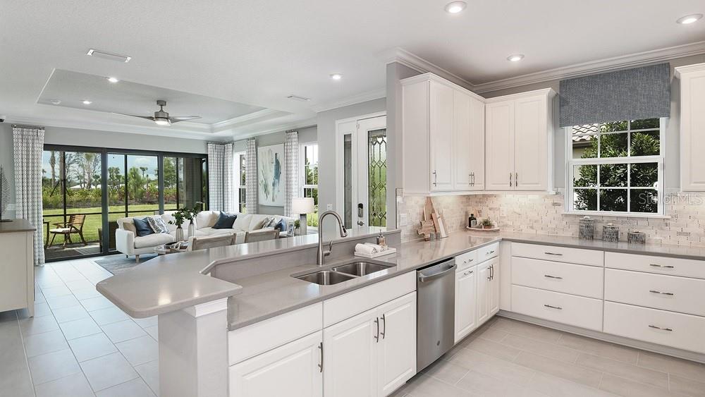 A modern kitchen with white cabinets and quartz countertops overlooks a bright, open-concept living area — 3224 TORTA COURT, BRADENTON, FL