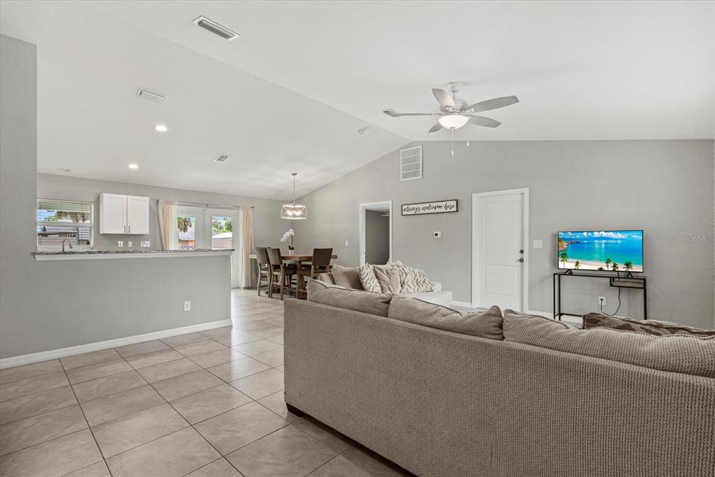 A living room with tile flooring, a large sectional sofa, and an open-concept dining area — 11481 WILLMINGTON BOULEVARD, PORT CHARLOTTE, FL