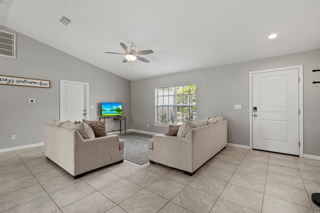 A living room features light gray walls, tile flooring, two sofas, and a ceiling fan — 11481 WILLMINGTON BOULEVARD, PORT CHARLOTTE, FL
