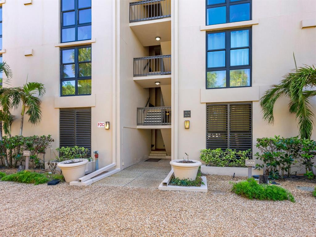 Exterior view of a multi-story apartment building with a central stairwell and two large planters — 22 SANDY COVE ROAD APT 203, SARASOTA, FL