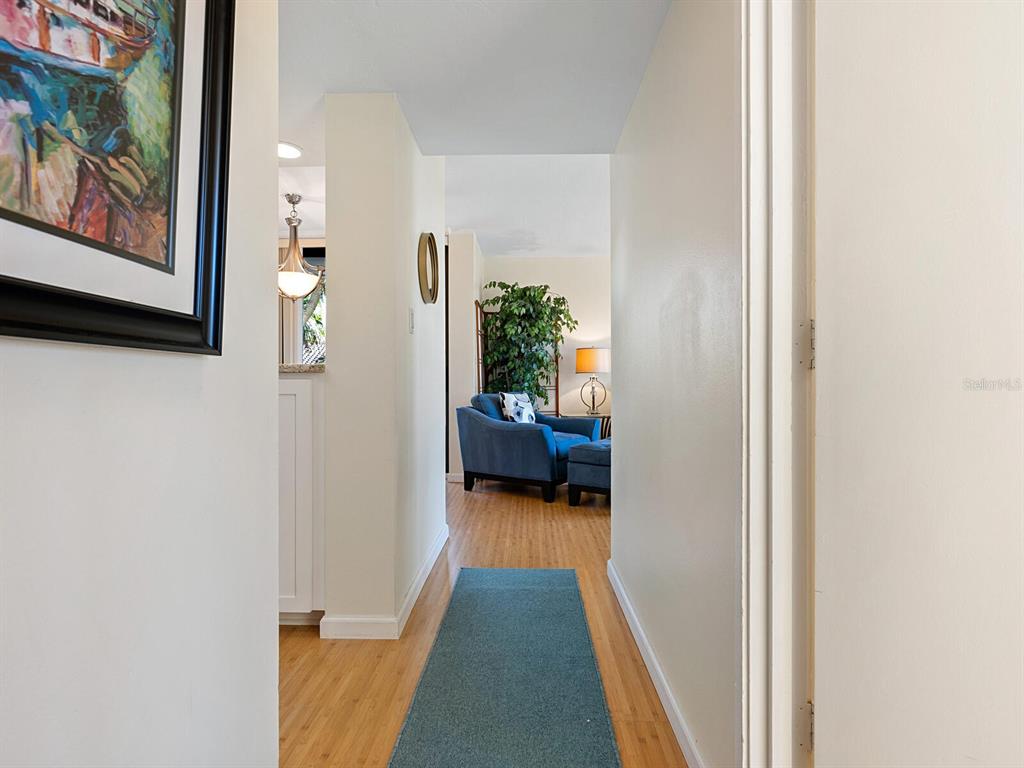 A hallway with light wood flooring and a blue runner leads to a living area — 22 SANDY COVE ROAD APT 203, SARASOTA, FL