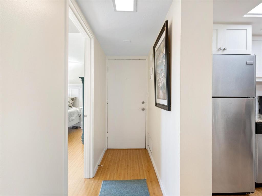 A hallway with wood flooring leads to a white door, with a kitchen refrigerator nearby — 22 SANDY COVE ROAD APT 203, SARASOTA, FL