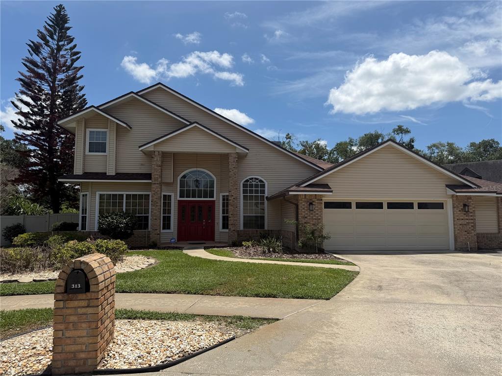 A two-story suburban house with tan siding, a red front door, and a two-car garage — 313 MACARTHUR PLACE, MAITLAND, FL