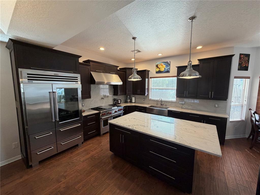 A kitchen features dark wood cabinets, stainless steel appliances, and a white marble-topped island — 313 MACARTHUR PLACE, MAITLAND, FL