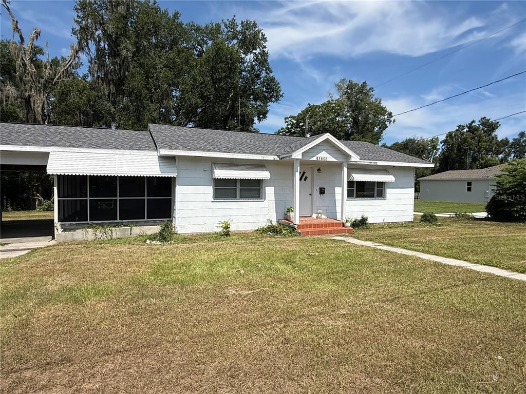 A single-story white house features a carport, a screened porch, and a front walkway — 13725 10TH STREET, DADE CITY, FL