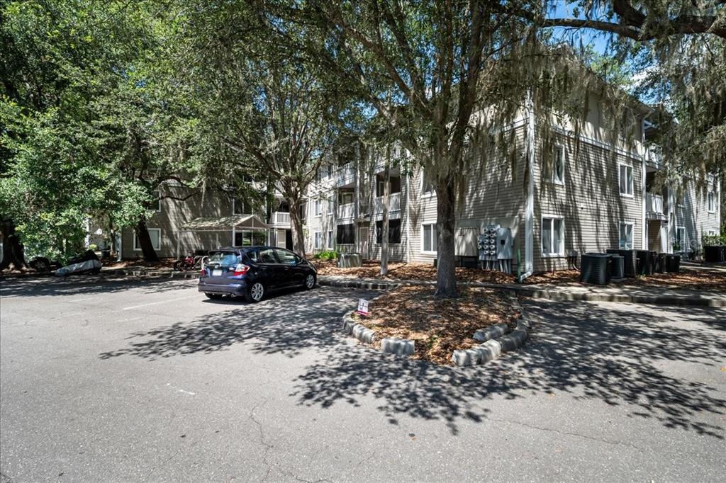 A multi-story apartment building with beige siding stands behind a parking lot and trees — 4000 SW 23RD STREET UNIT 4-305, GAINESVILLE, FL