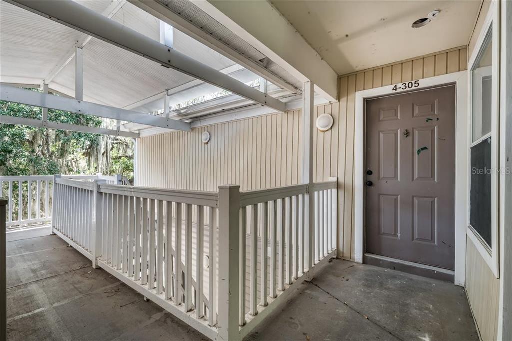 A covered outdoor walkway leads to the entrance of a residential unit numbered 4-305 — 4000 SW 23RD STREET UNIT 4-305, GAINESVILLE, FL