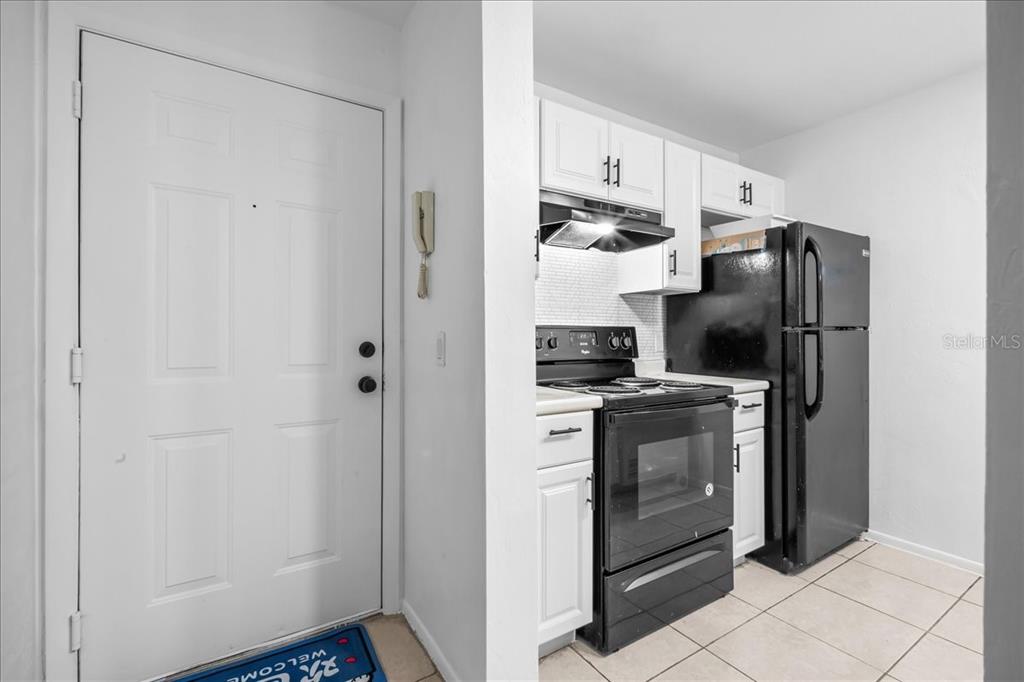 A white front door opens into a small kitchen with white cabinets and black appliances — 4000 SW 23RD STREET UNIT 4-305, GAINESVILLE, FL