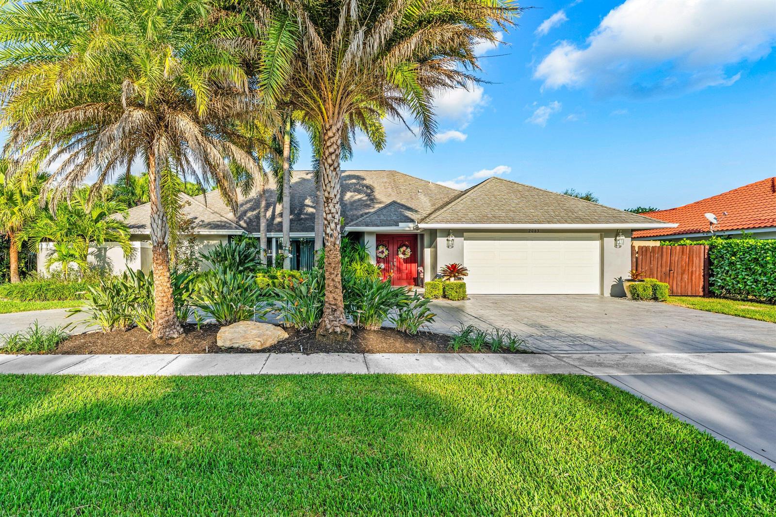 A single-story house with a white garage, red double front doors, and palm trees — 2063 Amesbury Circle, Wellington FL 33414, WELLINGTON, FL