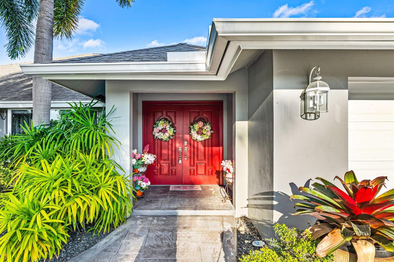 A house exterior features a red double front door with floral wreaths and tropical landscaping — 2063 Amesbury Circle, Wellington FL 33414, WELLINGTON, FL