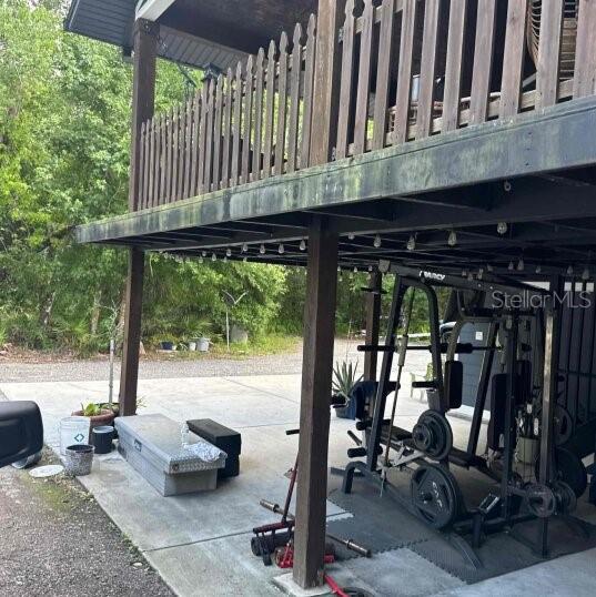 A home gym is set up on a concrete patio beneath an elevated wooden deck — 9931 BERRY DEASE ROAD, ORLANDO, FL