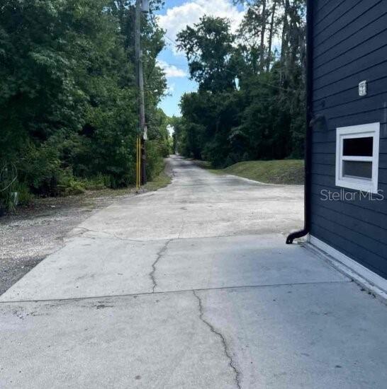 A concrete driveway leads past the side of a dark-sided building toward a wooded area — 9931 BERRY DEASE ROAD, ORLANDO, FL