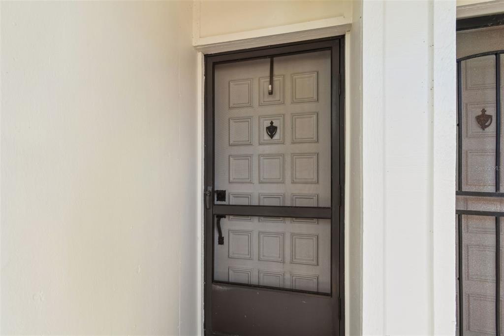 A close-up view of a dark metal screen door installed on a white exterior wall — 6105 PALMA DEL MAR BOULEVARD S UNIT 120, ST PETERSBURG, FL