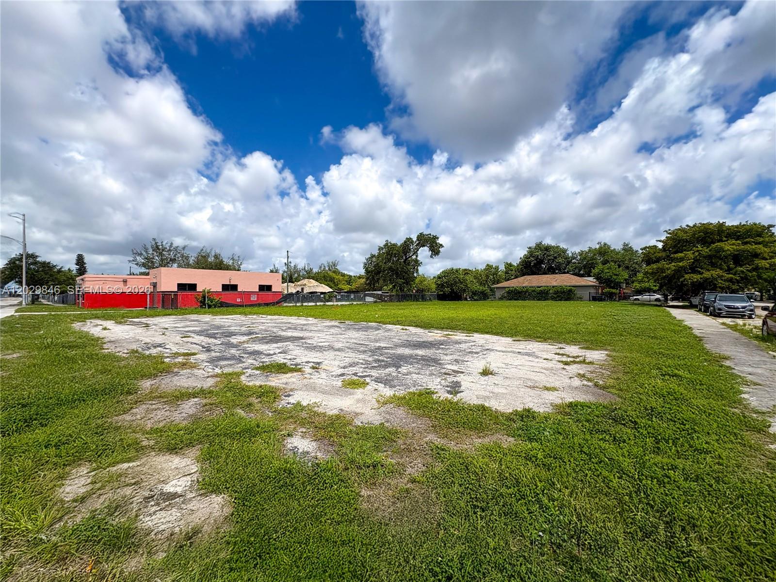 A vacant, grassy lot features a large, weathered concrete slab under a cloudy blue sky — 7920 NW 11th Ave, Miami FL 33150, MIAMI, FL