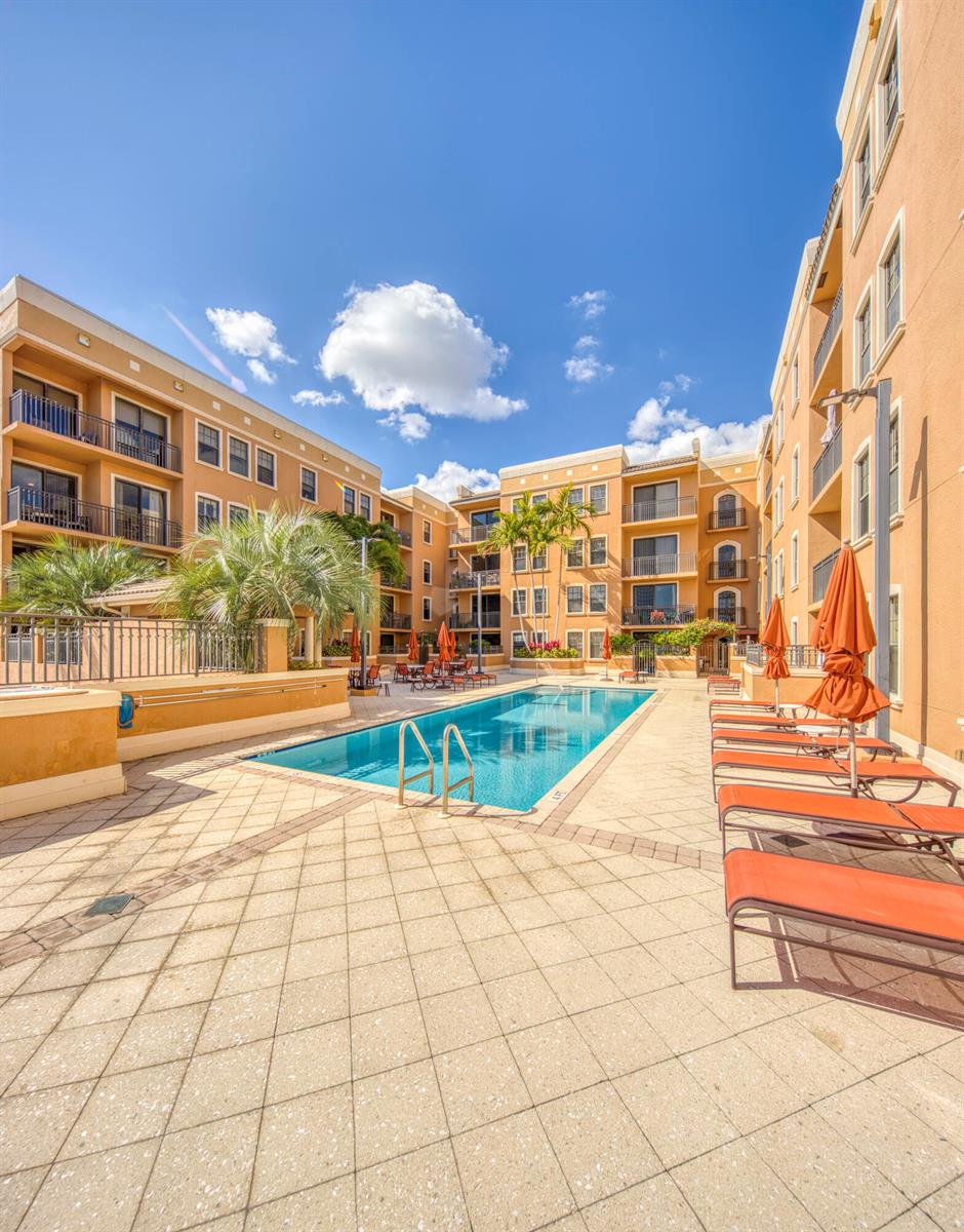 A rectangular swimming pool is surrounded by lounge chairs and umbrellas in a courtyard — 511 Lucerne Avenue # 401, FL 33460, FL