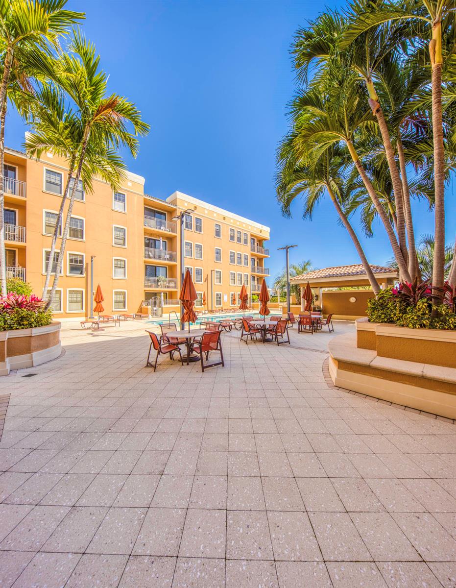 An outdoor patio area features dining tables with umbrellas, palm trees, and a multi-story building — 511 Lucerne Avenue # 401, FL 33460, FL