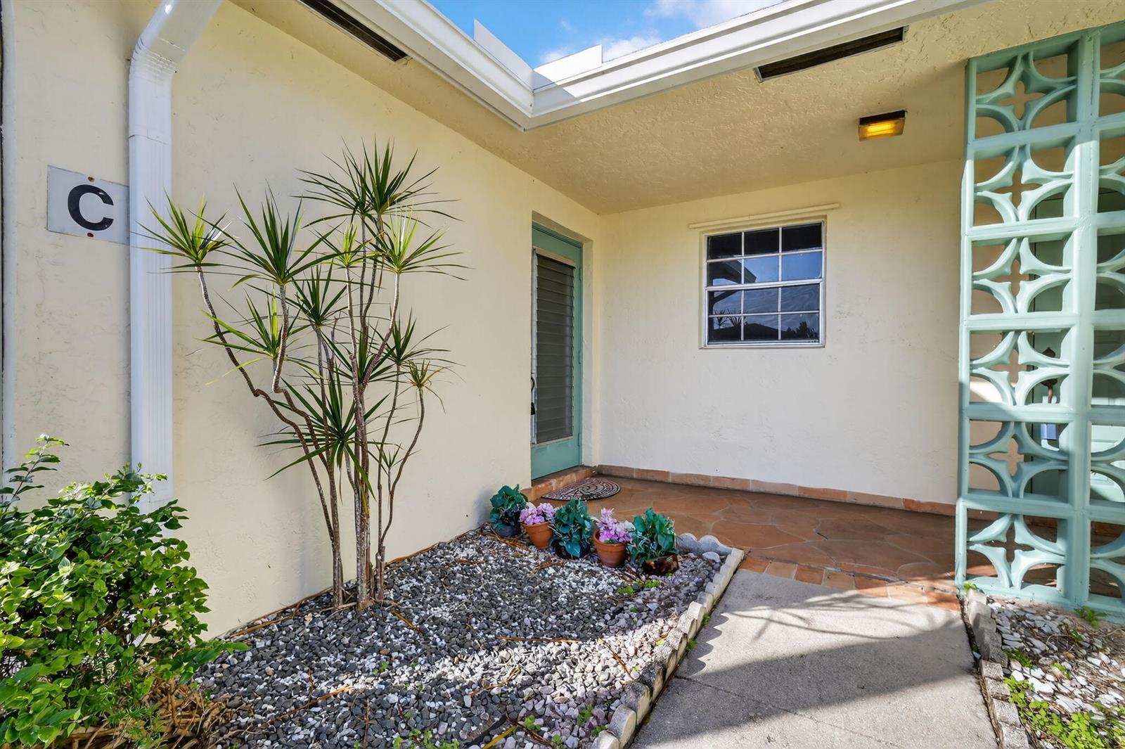 An exterior view of a building entrance featuring a gravel garden, potted plants, and breeze blocks — 5091 Lakefront Boulevard # C, Delray Beach FL 33484, DELRAY BEACH, FL