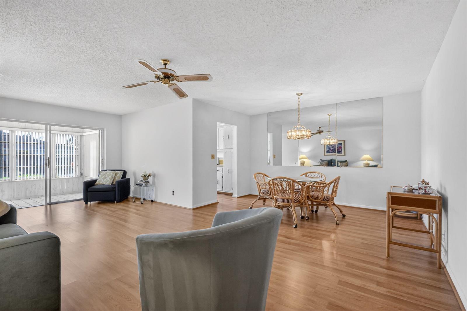 A living and dining area with wood-look flooring, a ceiling fan, and a mirrored wall — 5091 Lakefront Boulevard # C, Delray Beach FL 33484, DELRAY BEACH, FL